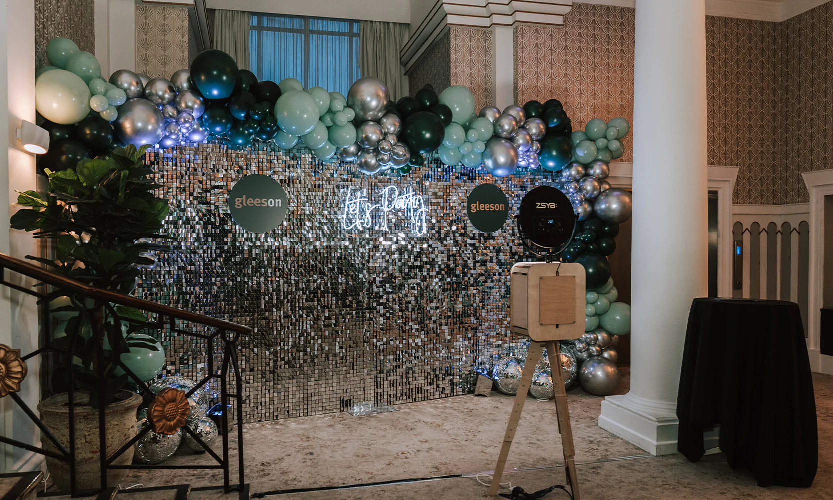Corporate event set up featuring unmanned photo booth, silver sequin wall, neon sign, corporate balloons and custom acrylic disc with company logo.