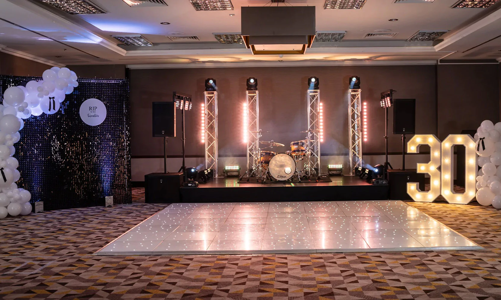 White LED dance floor at a wedding venue with sequin wall, white light-up numbers and balloons.