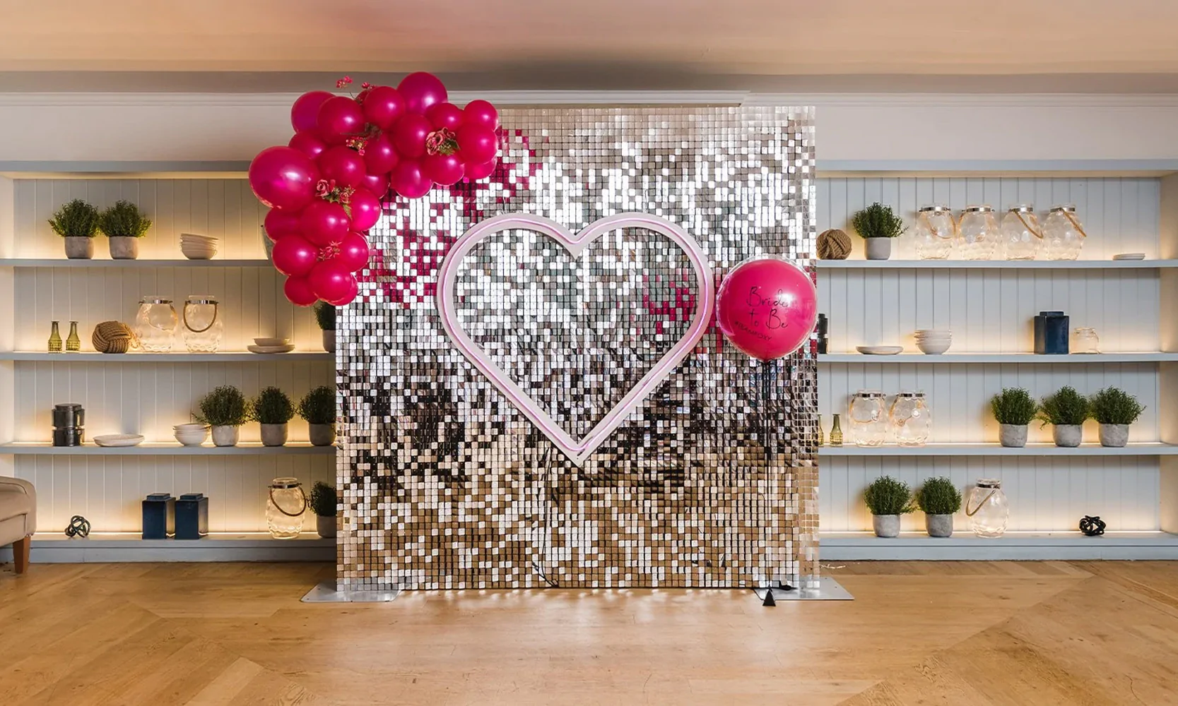 Silver sequin wall with neon love heart and red balloons.