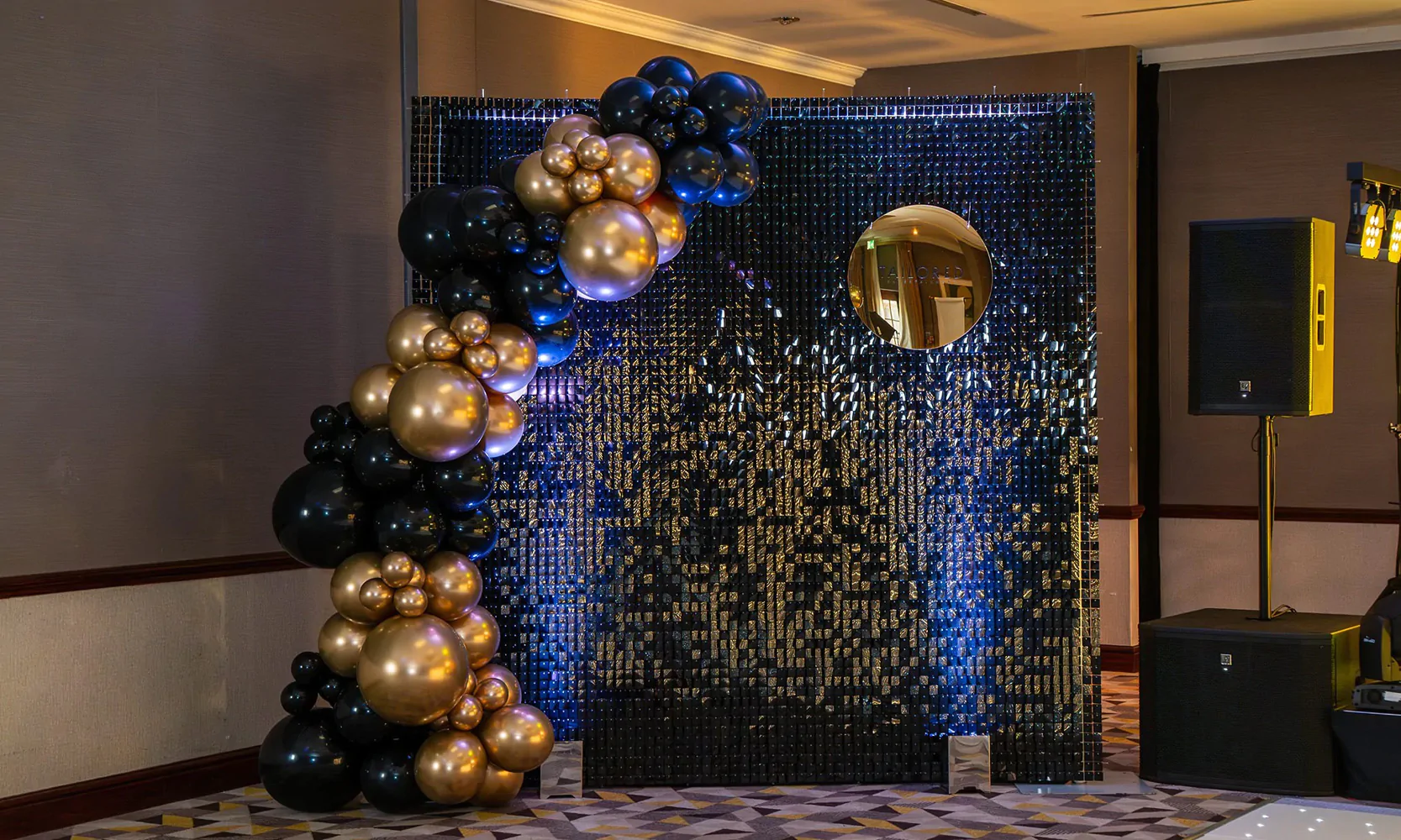 Sequin wall with uplighters and gold and blue balloons.