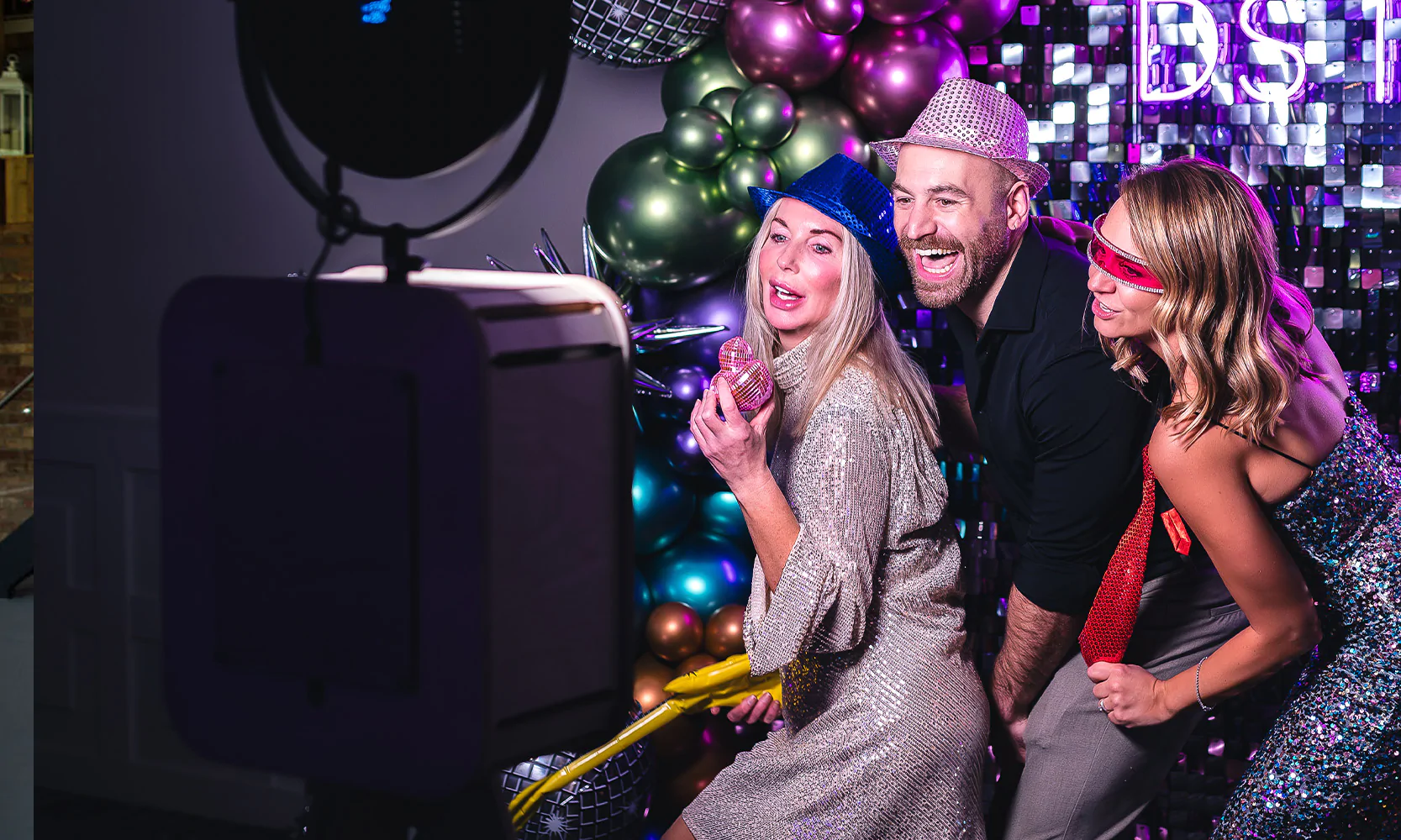 Guests enjoying party featuring unmanned photo booth, custom neon sign and sequin wall backdrop.